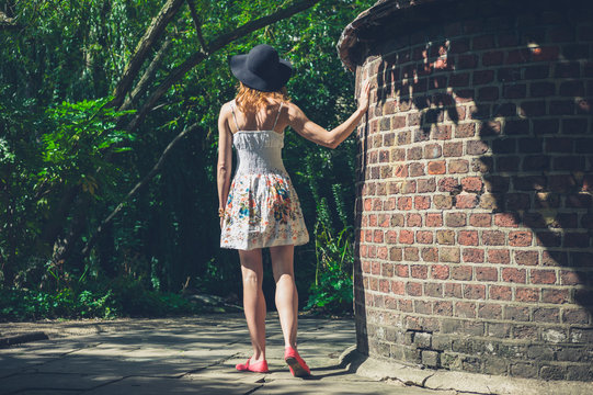 Young woman in dress and hat by brick wall