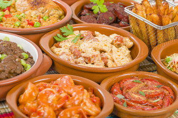 Tapas - Selection of latin dishes. Chorizo al vino, Higados de pollo, Chicken and chorizo, Tomates al ajillo, Arroz con pollo, Camarones enchilhados, Patatas a ala riojana and Stuffed mushrooms.
