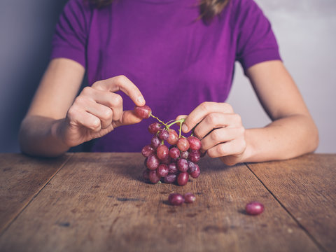 Young woman at table eating grapes