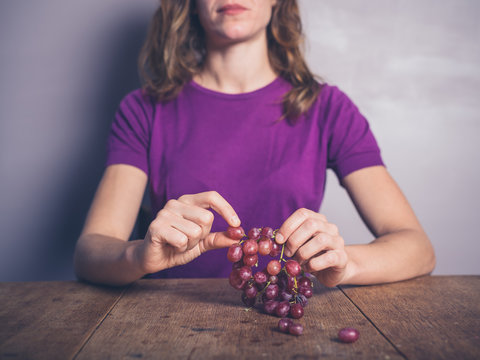 Young woman at table eating grapes