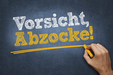 Hand schreibt mit Kreide Text "Vorsicht Abzocke!" auf Tafel
