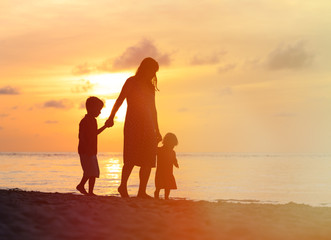 mother and two kids walking on beach at sunset