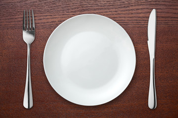 Fork and knife with white plate on wooden table