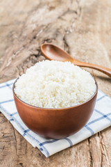 Cooked rice in bowl with spoon and dishcloth on old wooden table