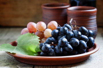 Blue and pink grapes on a clay plate and wine in rustic style, s