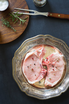 Raw pork rib chops on the metal plate with spices and herbs