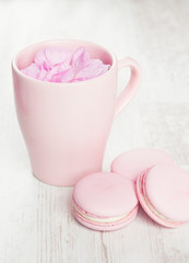 Obraz na płótnie Canvas Tender pink macaroons and tea cup on white wood background