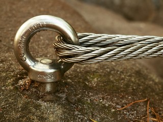 Detail of steel bolt anchor eye in rock. The end knot  of steel rope. Climbers path in rocks via...