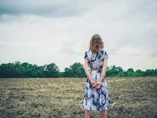 Young woman standing in barren field on cloudy day