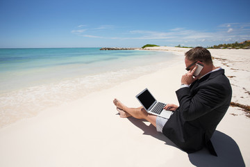 Businessman on the beach working with computer and speaking on