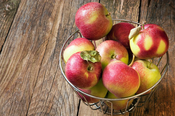 Apples in a metal basket on a wooden table.