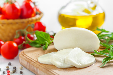Mozzarella cheese sliced on board, fresh tomatoes, basil and arugula on table