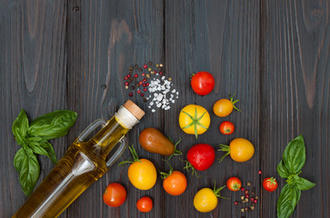 Cherry tomatoes of various color, basil leaves, spices and olive oil from above over dark wooden table. Italian caprese salad recipe ingredients. Top view, free text copy space