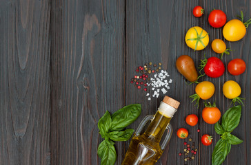 Cherry tomatoes of various color, basil leaves, spices and olive oil from above over dark wooden table. Italian caprese salad recipe ingredients. Top view, free text copy space