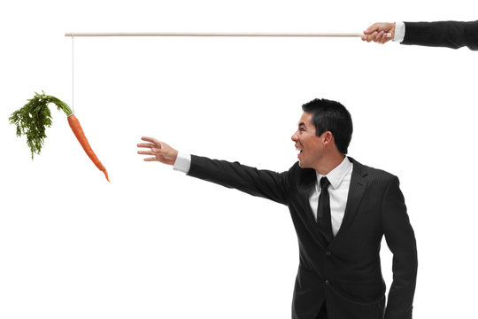 Excited businessman reaching for a carrot on the end of a stick