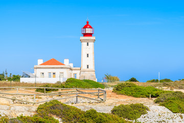 Fototapeta na wymiar Lighthouse building on top of cliff on coast of Portugal near Carvoeiro town