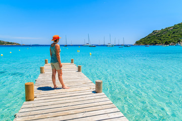 Young woman tourist standing on wooden jetty on Santa Giulia beach looking at azure sea, Corsica island, France