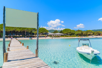 Wooden jetty on Santa Giulia beach with dinghy boat on azure sea, Corsica island, France