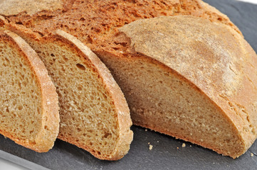 Sliced home-baked bread made using Natural Starter and organic wholegrain wheat flour on a black slate plate (tray). Healthy food concept.
