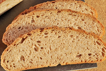 Three slices of fresh home-baked traditional Silesian dark bread made using Natural Starter and organic wholegrain wheat and rye flour on a black square slate plate (tray). Healthy food concept.