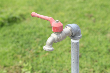 close up of water faucet with green grass background - Selective