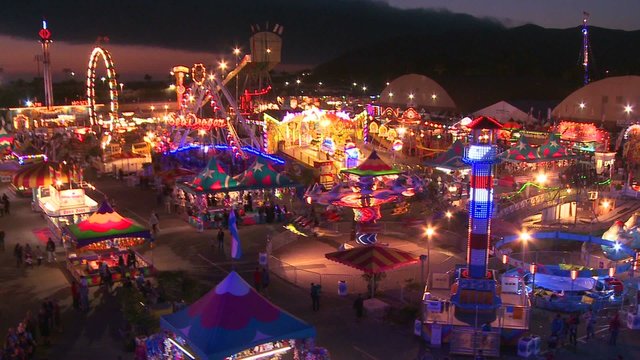 A high angle view over a brightly lit amusement park with many rides and attractions.