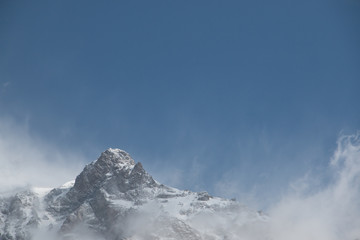 Top of a snow mountain surrounded by clouds and blue sky