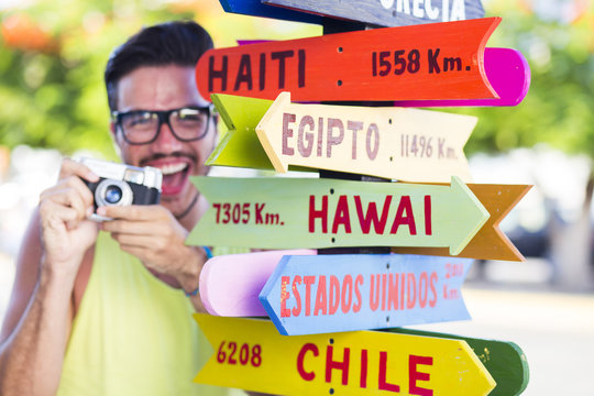 Colorful picture of a hipster young man in holidays taking pictures next to a destination sign