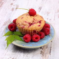 Fresh baked cupcake and raspberries on plate on old wooden background, delicious dessert
