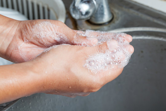 Woman washing her hands with soap over sink in kitchen room