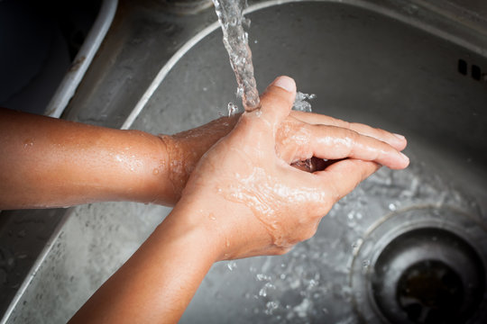Woman washing her hands under running water in kitchen room