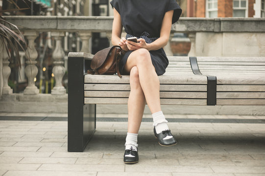 Young woman on bench in city with phone