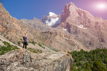 Fototapeta na wymiar Young Woman Staying on Rock with Arms Raised Up Female body on top of Stone Stretching body Towards Sun morning mountain landscape background Shining Sun