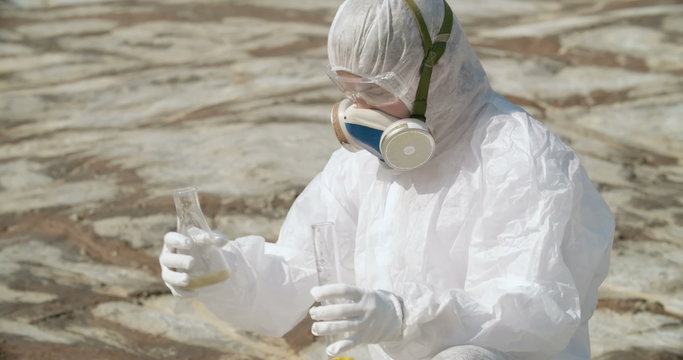 Female researcher in protective clothing making experiment in arid hazardous area