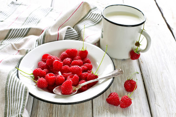 Raspberries in plate with cup of milk on wooden background