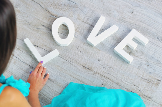 Woman puts together wooden decoration letters into love word on the floor, top view