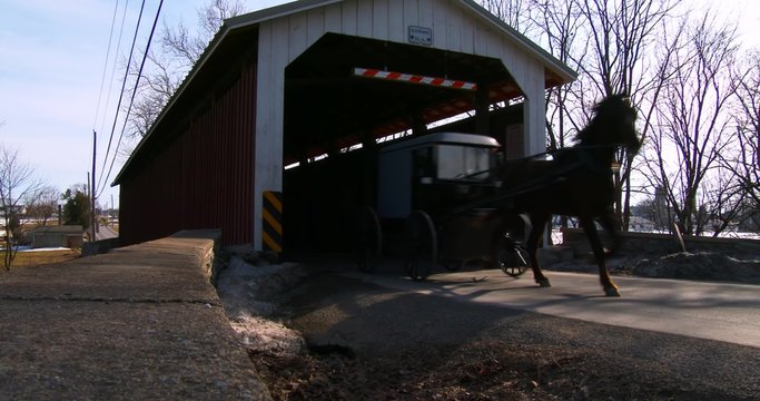 An Amish horse cart travels through a covered bridge along a road in rural Pennsylvania.