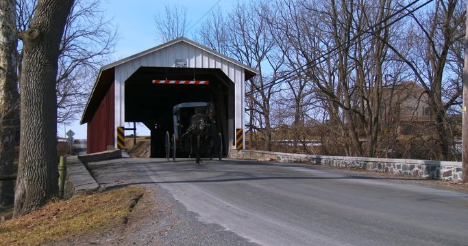 An Amish horse cart travels through a covered bridge along a road in rural Pennsylvania.