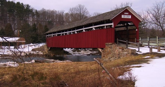 A pretty red covered bridge over a river in winter.