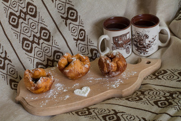 Three donuts with cherry on the cutting board with sugar heart.  Two cups with tea. Her cup is with flowers, and him cup is with car. Romantic breakfast.