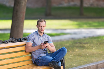 Obraz premium Young man sitting in the park with a smart phone