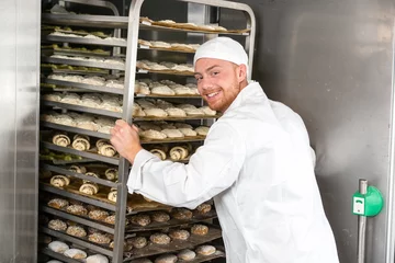 Schilderijen op glas Baker at bakery putting rack of fresh dough in refrigerator © ikonoklast_hh