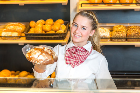Shopkeeper in bakery presenting loaf of bread to client
