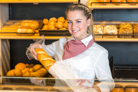 Shopkeeper at bakery putting loaf of bread into paper bag