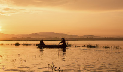 Silhouette of fisherman rowing boat on reservoir in the morning