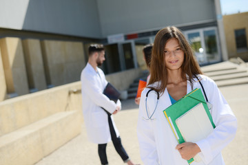 portrait of an attractive cheerful young medical student woman outdoor in front of hospital university campus
