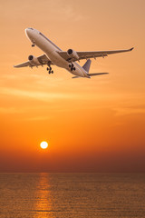 Commercial airplane flying over the sea at sunset