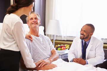 Doctor Talking To Male Patient And Wife In Hospital Bed