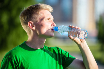 Tired man drinking water from a plastic bottle after fitness