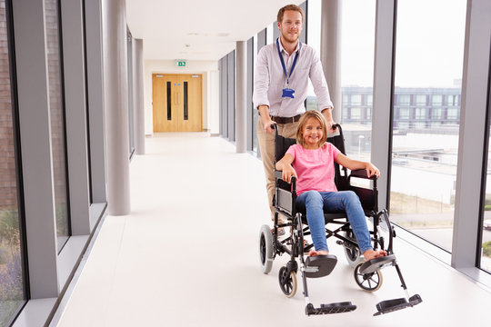 Doctor Pushing Girl In Wheelchair Along Corridor